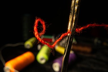 Siyah zemin üzerinde kırmızı iplik ve renkli iplik makaraları olan iğne gözü. Permetasyon iplikli çelik terzi iğnesi. Dikiş dikmek, nakış işlemek, giysilerin tamiri için bir araç..