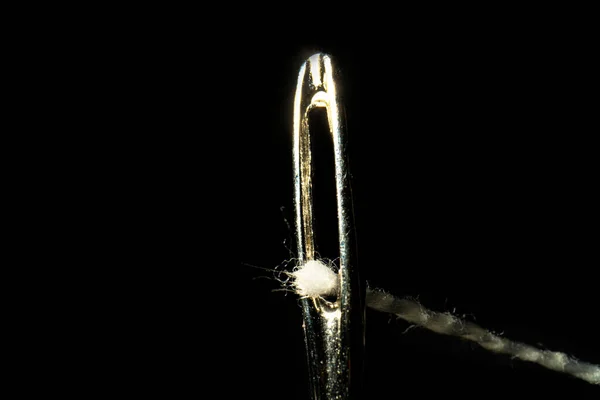 Macro image of a needle eye threaded with piece of white thread on black background. Steel shiny tailors needle with permeation thread close up. The tool for sewing, embroidery, repair of clothes. — ストック写真