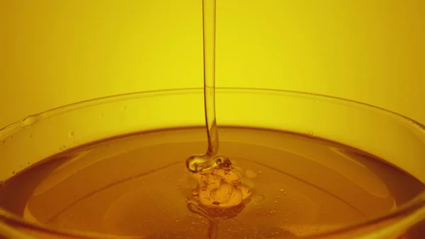 Honey dripping, pouring from spoon in glass. Thick honey molasses dripping into full glass. Close up of golden honey liquid, sweet product of beekeeping. Sugar syrup is pouring on yellow background. — Foto de Stock