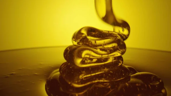 Honey dripping, pouring thick stream on yellow background. Viscous honey molasses flowing. Close up of golden honey liquid, sweet product of beekeeping. Sugar syrup is pouring flow. – stockfoto