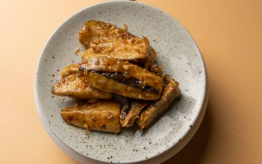 Karamelize edilmiş kızarmış muzlar kahverengi arka planda yuvarlak gri bir tabakta sunuluyor. Tereyağı ve şekerle kızartılmış muz parçaları. Restoranda yemek servisi, tatlı Tayland tatlıları. Asya mutfağı