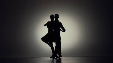 İki profesyonel balo dansçısı tarafından gerçekleştirilen tutkulu tango koreografisi. Gri arka planda arka planda hareket eden bir erkek ve bir kadının siyah siluetleri. Duygular, aşk, romantizm