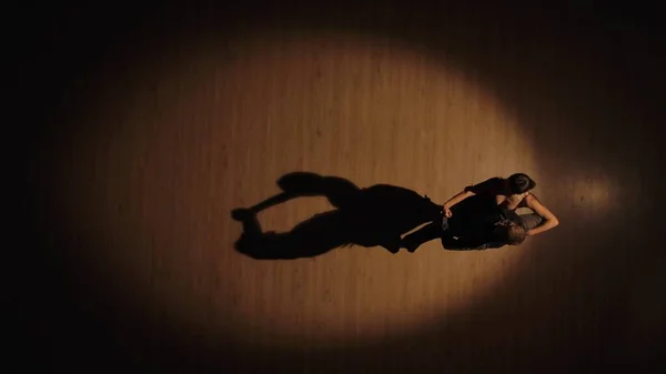 Top view of a couple of ballroom dancers dancing Argentine tango elements on a parquet floor with dancing shadows. Passionate movements of partners on Latin dancing on a brown background. Slow motion