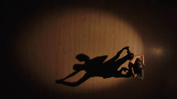 ダンスの影を持つ寄木細工の床の上にアルゼンチンタンゴの要素を踊るいくつかのボールルームダンサーのトップビュー 茶色の背景でラテンダンスのパートナーの情熱的な動き スローモーション — ストック写真