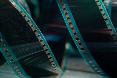 Yumuşak yeşil ışıkta ahşap yüzeyde sarmal retro film şeridi. Çarpık analog eski film şeritleri fotoğraf ya da video kamera için yakın çekim. Sinematografi, fotoğrafçılık, fotografik hafıza kavramı.