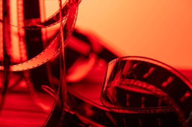 Yumuşak kırmızı ışıkta klasik film şeridi. Bir fotoğraf ya da video kamera için eski film şeritleri bükülmüş. Sinematografi, fotoğrafçılık, fotografik hafıza kavramı.