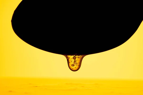 Honey dripping, pouring from dark spoon on yellow background. Thick viscous honey molasses flowing. Close up of golden honey liquid, sweet product of beekeeping. Sugar syrup is pouring. Healthy and