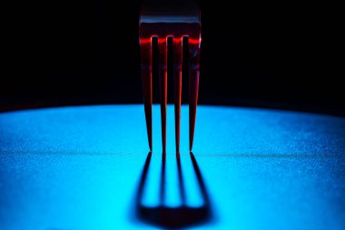 Dişleri olan bir çatalın parçası siyah arka planda mavi masa yüzeyine koyu gölgeler bırakıyor. Mutfak çatal bıçakları kapansın. Çatal bıçak, mutfak gereçleri, bulaşık takımı, yemek takımı, restoranlar için servis ya da