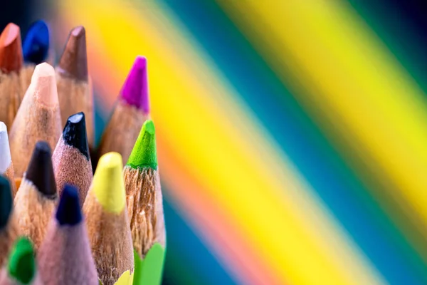Background of colorful sharpened colored pencils against the backdrop of a painted rainbow. Multicolored wooden pencils close up. Stationery set for drawing, coloring. Art school, tool for creativity
