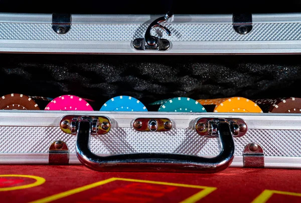 An open suitcase with a set of multicolored casino chips on a red gambling table. Gambling background in roulette, poker, blackjack. Jackpot, money, bets, win. Close up