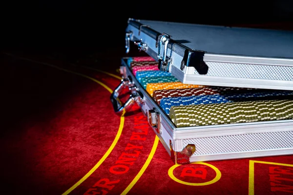 An open suitcase with a set of multicolored casino chips on a red gambling table. Gambling background in roulette, poker, blackjack. Jackpot, money, bets, win. Close up