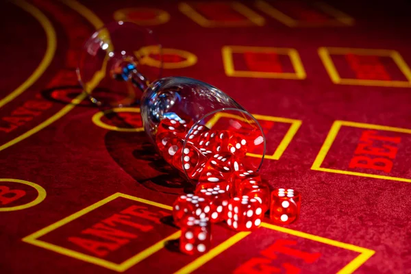 A fallen glass of champagne with red dice scattered across the table. Close up of a set of dice for craps, roulette, poker on a red gaming table in a casino. Gambling background