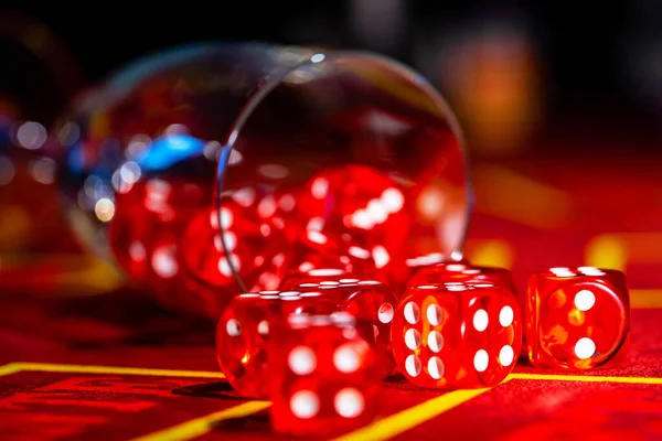 A fallen glass of champagne with red dice scattered across the table. Close up of a set of dice for craps, roulette, poker on a red gaming table in a casino. Gambling background