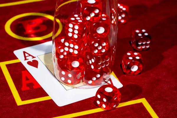A red casino table with an ace of hearts and a set of red dice in a glass. Close up of cards and dice for playing craps, poker or roulette. Gambling club. Game for money, bets, risk, success