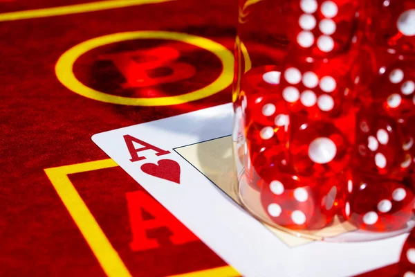 A red casino table with an ace of hearts and a set of red dice in a glass. Close up of cards and dice for playing craps, poker or roulette. Gambling club. Game for money, bets, risk, success