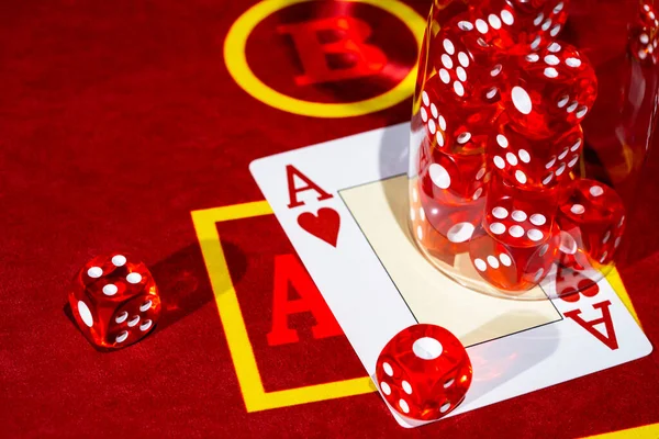 A red casino table with an ace of hearts and a set of red dice in a glass. Close up of cards and dice for playing craps, poker or roulette. Gambling club. Game for money, bets, risk, success