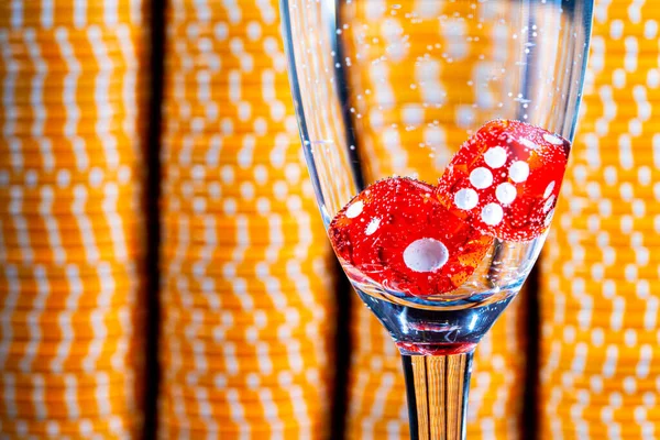 Red dice in a glass of champagne on a background of yellow casino chips. Close-up of dice for playing craps, poker. Gambling background in casino, entertainment club, success