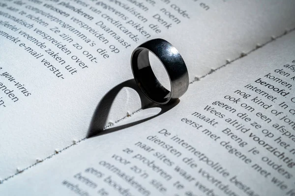 Silver old ring casts heart shaped shadow in book. Shadow of heart made from wedding band in book close up. Concept of relationship, proposal, wedding, valentines day gift. Love and feelings