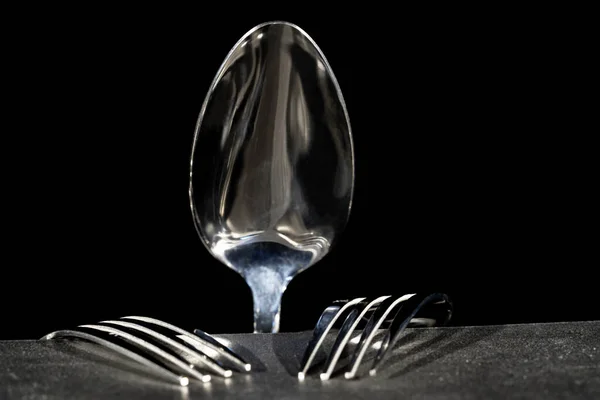 Spoon and two silver forks lying on gray table surface. Kitchenware utensil, silverware on a black background close up. Background of cutlery, serving for restaurants or cafes. Dishes for food, dinner