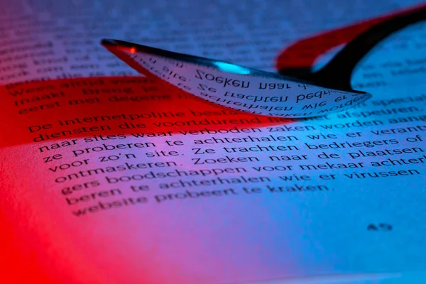 Reflection of printed text on the back of a steel spoon. Text on a spoon close up. White sheets of a paper book in blue red light with words, symbols, printed font. Background of cutlery and book