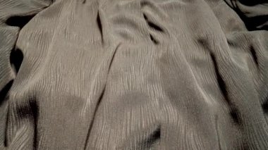 Parlak gri kumaşın detaylı kumaş dokusu, makro yakın görüntüde doli çekimle birlikte akıyor. Dalgalı, yoğun desenli malzeme. Kumaş, tekstil malzemesi. Tekstil soyut arka planı. Kıyafet ve moda