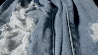 Delikleri ve aşınmaları olan kot pantolon kumaşı. Giysinin yapısı, tekstil malzemesi, pamuktan kumaş. Kumaş kumaş dokusuna çok yakın. Moda, tekstil