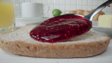 Bir kaşık ekmek ekmeğine ahududu reçeli döküyor. Tatlı reçelli bir sandviçe yaklaş. Sabahları mutfakta lezzetli bir kahvaltı hazırlıyorum. Tatlı, lezzetli, fast food.
