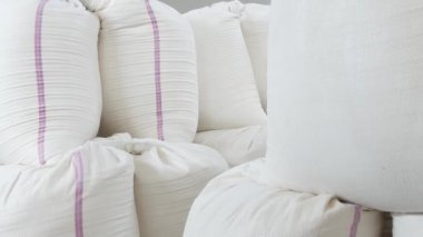 Üretim deposunda un, şeker, grat veya makarna içeren beyaz çuvallar. Bir endüstriyel girişimin deposunda paketlenmiş malların depolanması. Büyük, parlak bir depoda depolanmış bir çanta dolusu ürün.