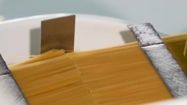 Makarna fabrikası ve makarna üretimi. Un ürünlerinden yapılan makarna. Spagetti üretim hattı boyunca hareket ediyor. Sıralar dolusu sarı renkli spagetti. Restoranlar ve kafeler için gıda arka planı