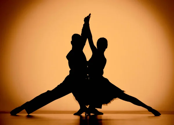 Couple of dancers are passionately dancing elements of Argentine tango. Black silhouettes of man and woman on an orange brown gradient background in studio. Screensaver for school of ballroom Latin