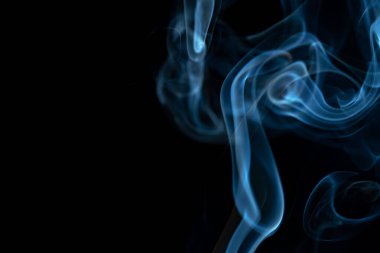 White blue cloud of smoke from smoking a cigar on an isolated black background. Fumes from smolder cigarette floating in the space. Smoke flying in the air and illuminated by light. Macro shot of