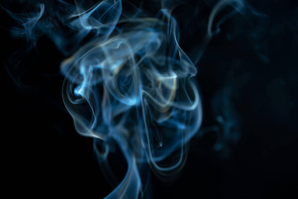White blue cloud of smoke from smoking a cigar on an isolated black background. Fumes from smolder cigarette floating in the space. Smoke flying in the air and illuminated by light. Macro shot of