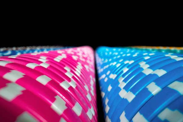 Vertical rows of colored casino chips on an isolated black background. Set of blue and pink gambling chips. The concept of a casino, playing poker, roulette or craps. Bet, money, win. Extra close up