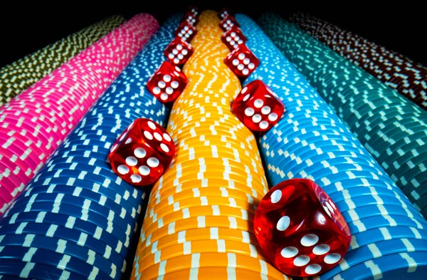 Vertical rows of colored casino chips and many red dice on isolated black background. Set of yellow, blue and pink gambling chips. Concept of casino, playing poker, roulette or craps. Bet, money, win