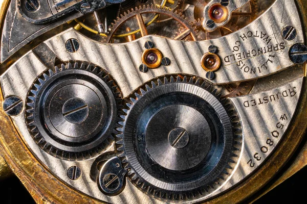 Rear viev of a old pocket watch with an open clockwork on black isolated background. Retro clock with engraving, inside view of gearing, gears. Mechanism of mechanical golden vintage watch close up