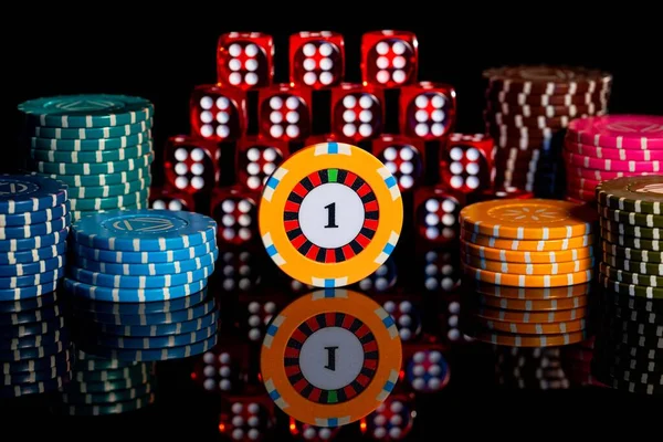 Куча красных кубиков и стопка фишек казино на изолированном черном фоне. Пирамида кубиков с шестью и чипом с блоком на отражающей поверхности стола. Основы азартных игр в казино. Крэпс, покер Лицензионные Стоковые Изображения