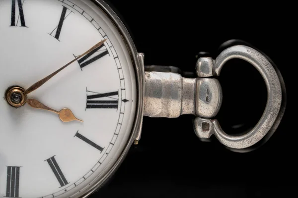 Part of a silver antique pocket watch dial with an eyelet for chain on a black isolated background. Retro clock with minute, hour hands and Roman numbers on a white clock face. Old timepiece close up