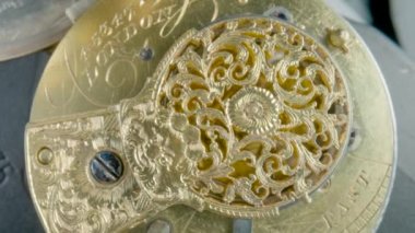 Clockwork mechanism macro. Round wheel with a carved pattern from curlicue on an antique gold clock. Old vintage clockwork working. Internal movement of watch with rotating spring and screws