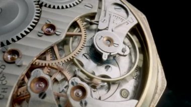 Antique pocket watch mechanism moving on isolated black studio background. Macro shot of clockwork with rotating spring, gears, cogwheel and wheels with tootheds. Disassembled silver retro pocket