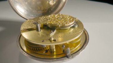 Clockwork mechanism with rotating spring, gears, gearing and toothed wheels. Round wheel with a carved pattern from curlicue on an antique gold clock. Old vintage clockwork working on a white