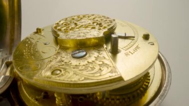 Clockwork mechanism with rotating spring, gears, gearing and toothed wheels. Round wheel with a carved pattern from curlicue on an antique gold clock. Old vintage clockwork working on a white