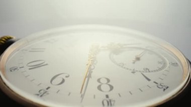 Beyaz kadranlı antika bir cep saati ve hareket eden elleri parlak bir ışıkta dönüyor. Eski bir saatin yüzü. Sayıları daha yakın. Yuvarlak mekanik klasik cep saati