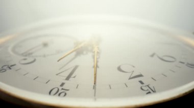 Antique pocket watch with a white dial and gold moving hands is spinning in bright light. The face of an old clock with numbers extra close up. Round mechanical vintage pocket watch
