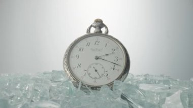 Antique silver pocket watch among shiny crystals or sparkling glass splinters. Round retro clock with a white dial, hands and numbers. Old vintage mechanical pocket watch on a light gray background