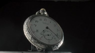 Siyah izole edilmiş bir arka planda dönen gümüş antika cep saati. Beyaz kadranlı, elleri ve numaraları olan yuvarlak gri retro saat. Eski model mekanik cep saati. Kapat.