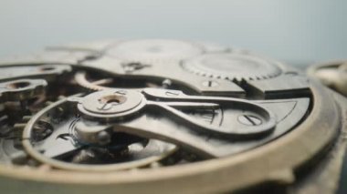 Macro shot of the internal parts of antique pocket watch on a light gray studio background. Clockwork with rotating spring, gears, cogwheel and tootheds wheels. Disassembled silver retro watch inside