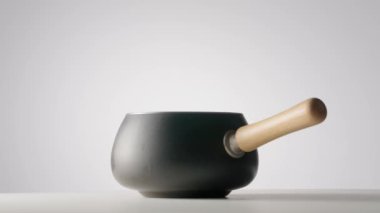Gray cast iron frying pan or saucepan with wooden handle rotating on light gray isolated background. Stainless steel cooking pot. Saucepan, stewpan, kitchen utensils. Deep frying pan. Fondue