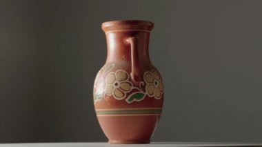 Brown jug with handle, handmade from clay with floral ornament rotating on dark gray studio background. Earthenware for drink and food. Kitchen utensils. Old rustic cookware made of earthen. Retro