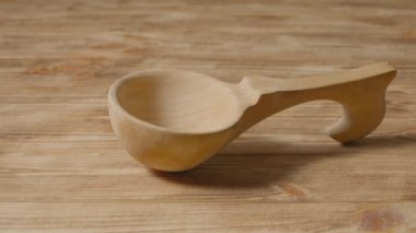 Camera pans over a wood spoon lying on a rustic wooden table. Carved wooden scoop. Old wooden utensils for eating soup. Empty ladle handmade from natural wood. Kitchenware, wood kitchen dipper