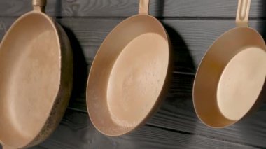 Restorandaki ya da evdeki ahşap gri mutfak duvarında asılı üç tane bakır kızartma tavası. Dolu boş altın tavaları ve sapları. Mutfak eşyaları, yemek ve kızartma için mutfak gereçleri, iç dekorasyon.